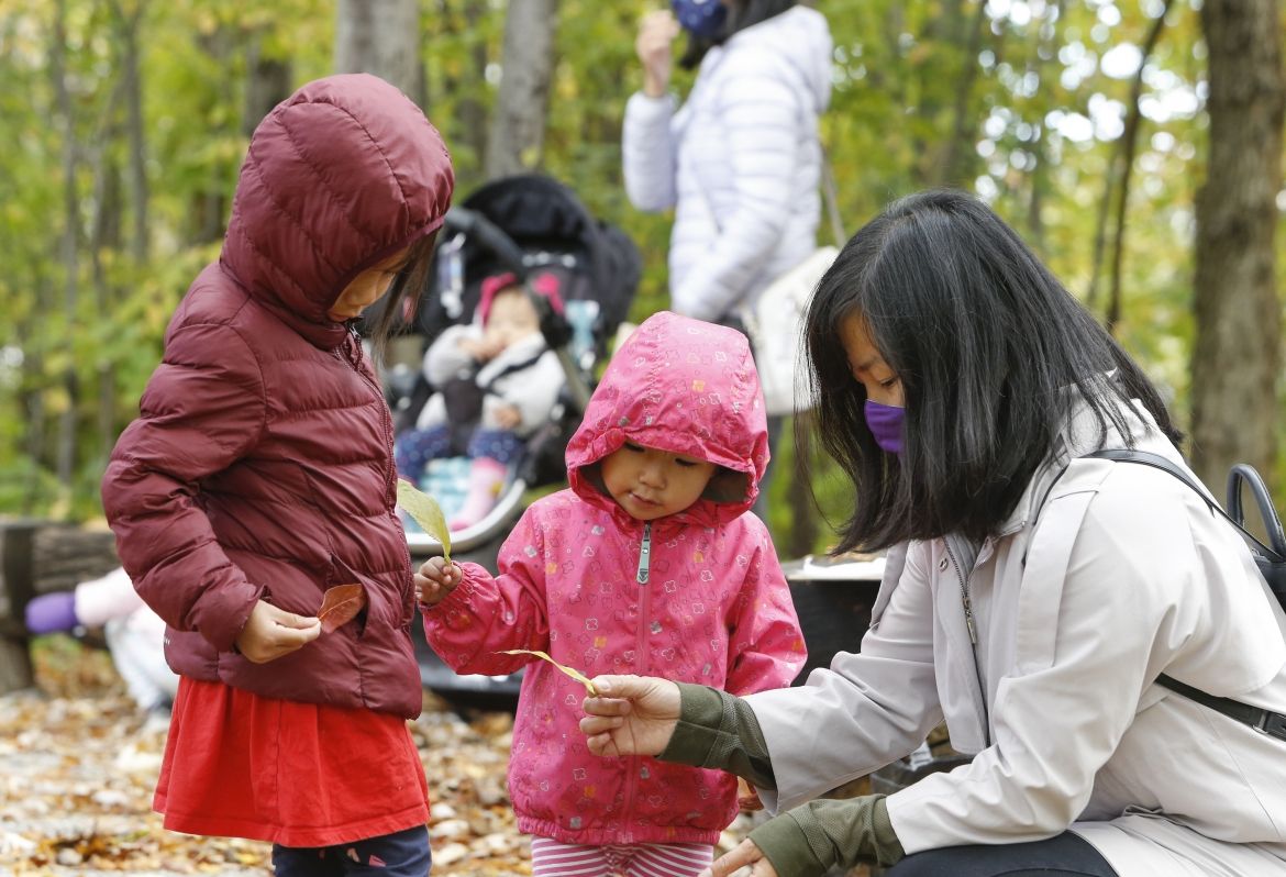 A caregiver and two kids playing with leaves.