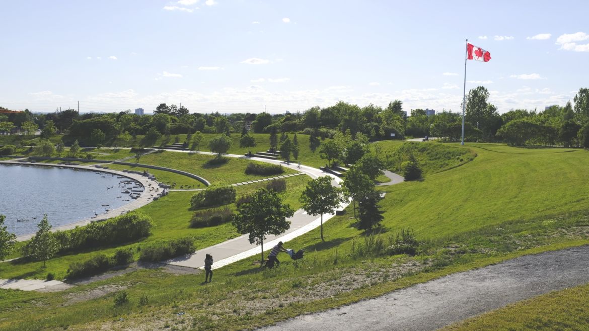The lake, a paved path, grass, trees, and a Canadian flag.