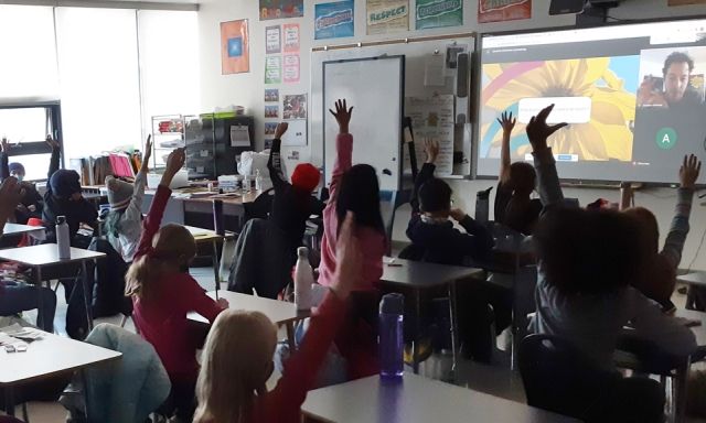 Kids raising their hands in a classroom. Downsview Park education staff are on the screen at the front of the class.