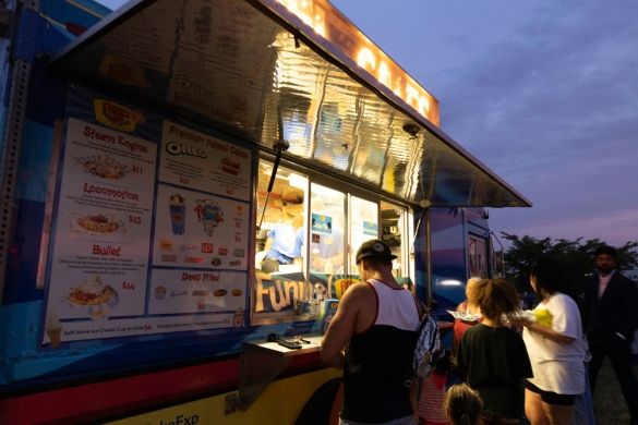 A funnel cake food truck illuminated against the night with customers in front