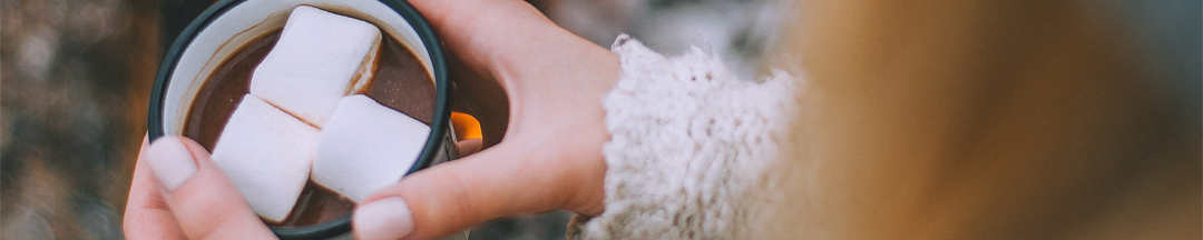 A person holding a mug of hot chocolate with marshmallows in it.