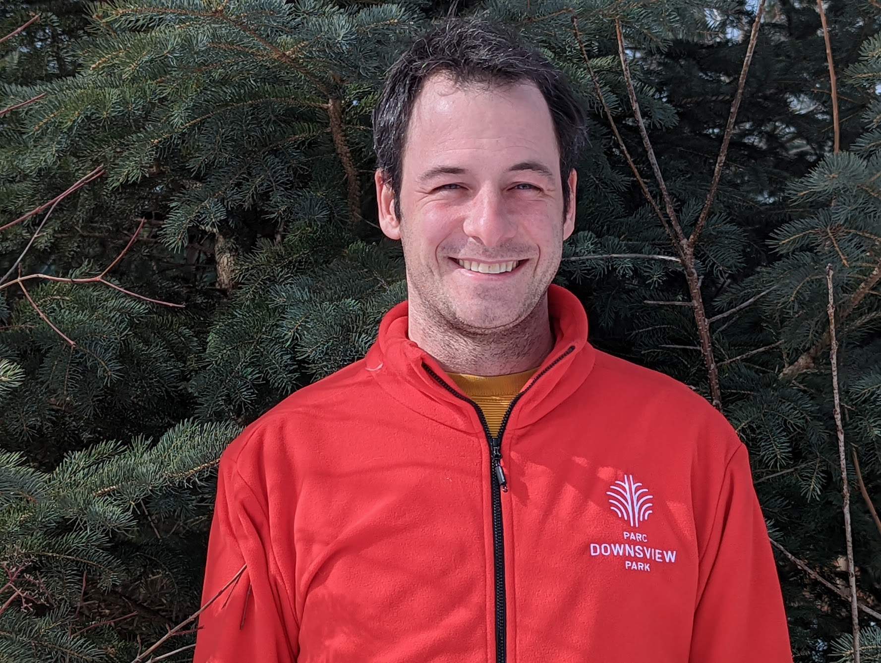 Jonny standing in the forest in a red Downsview Park zip-up.