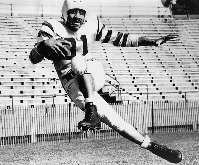 A black and white photo of football player Ulysses &quot;Crazy Legs&quot; Curtis in action during a game.
