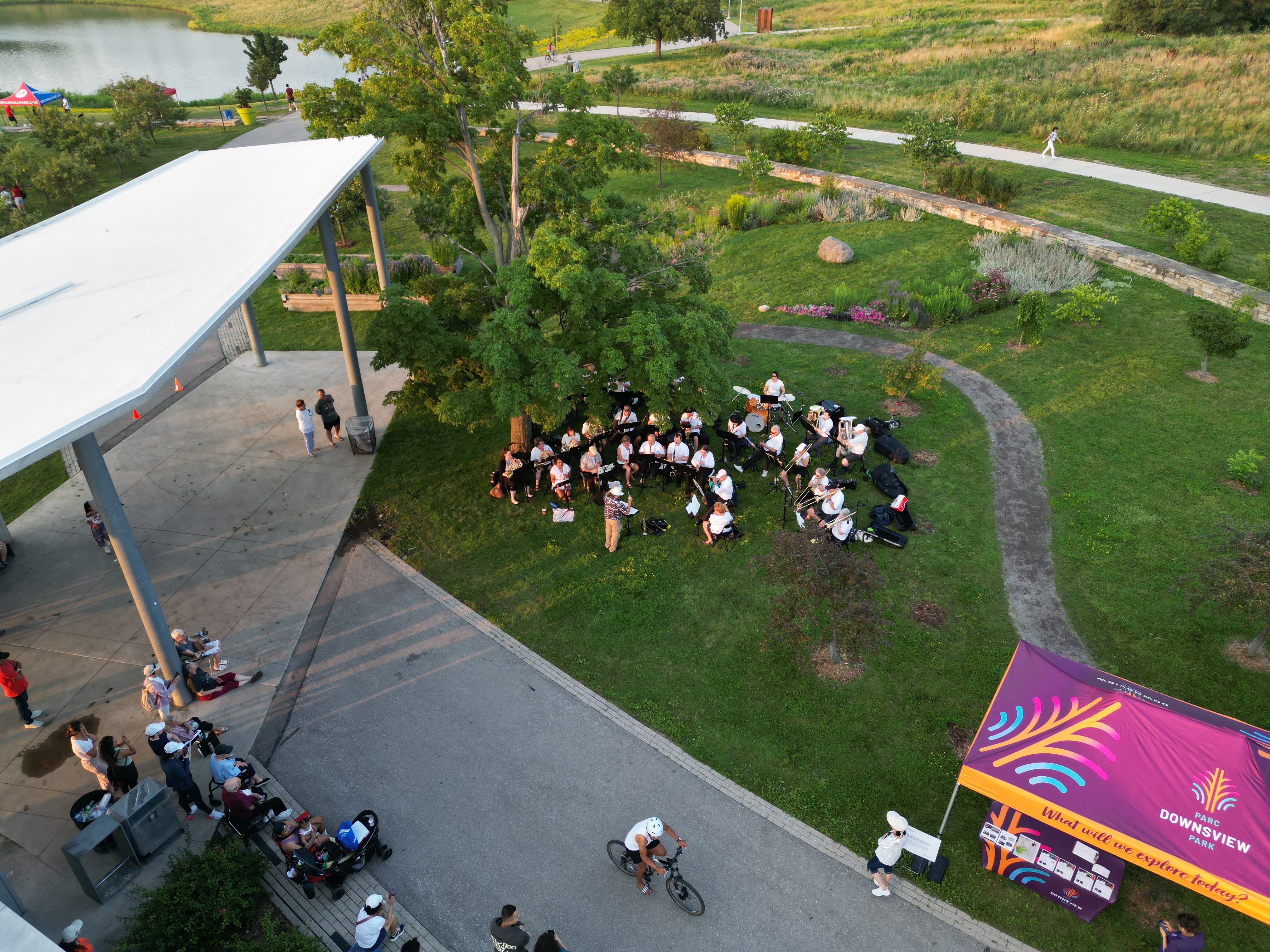 An orchestra sitting on chairs near a grassy area with an audience watching from the Orchard Pavilion