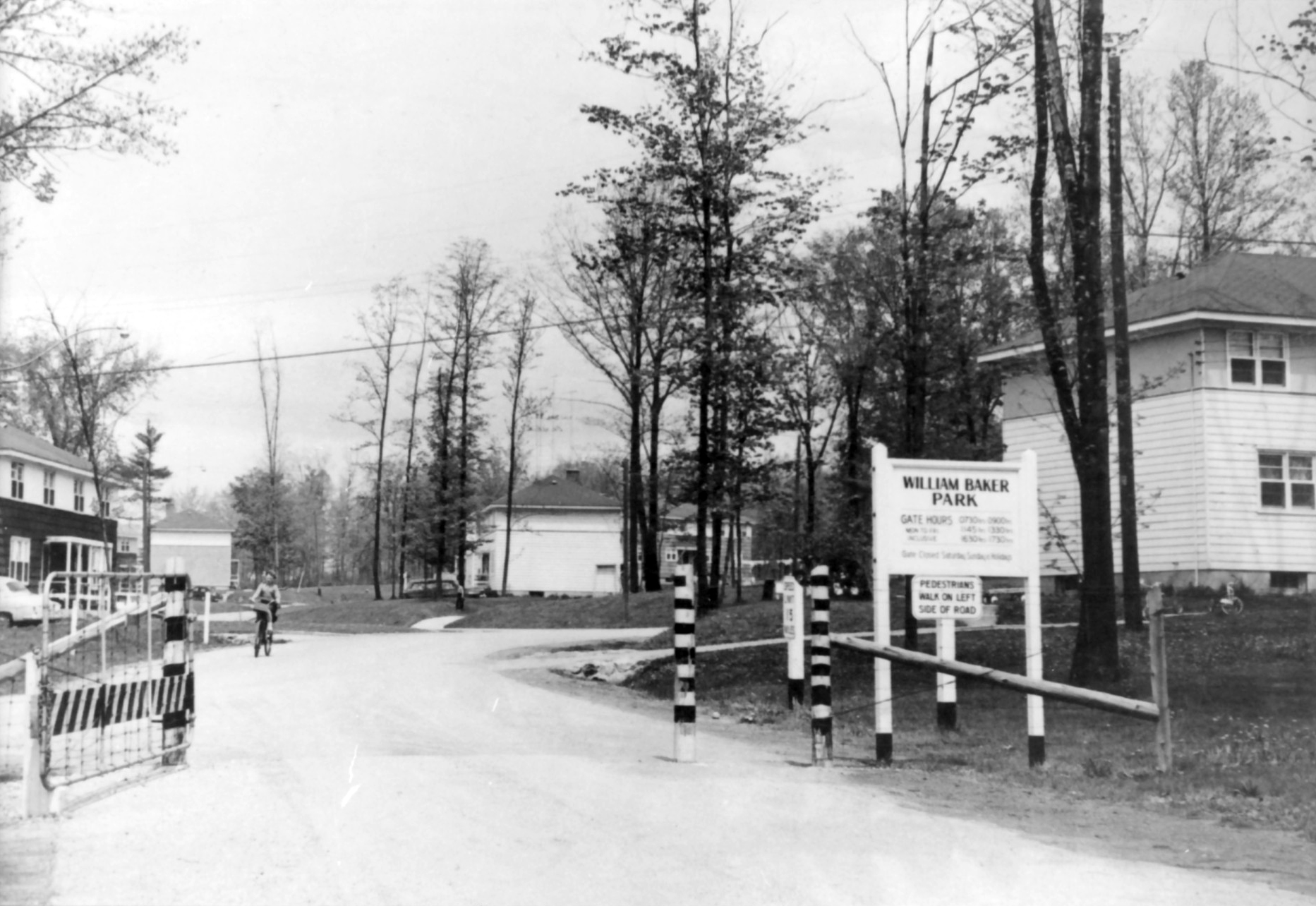 A kid biking along a neighbourhood road, next to a sign that says William Baker Park.