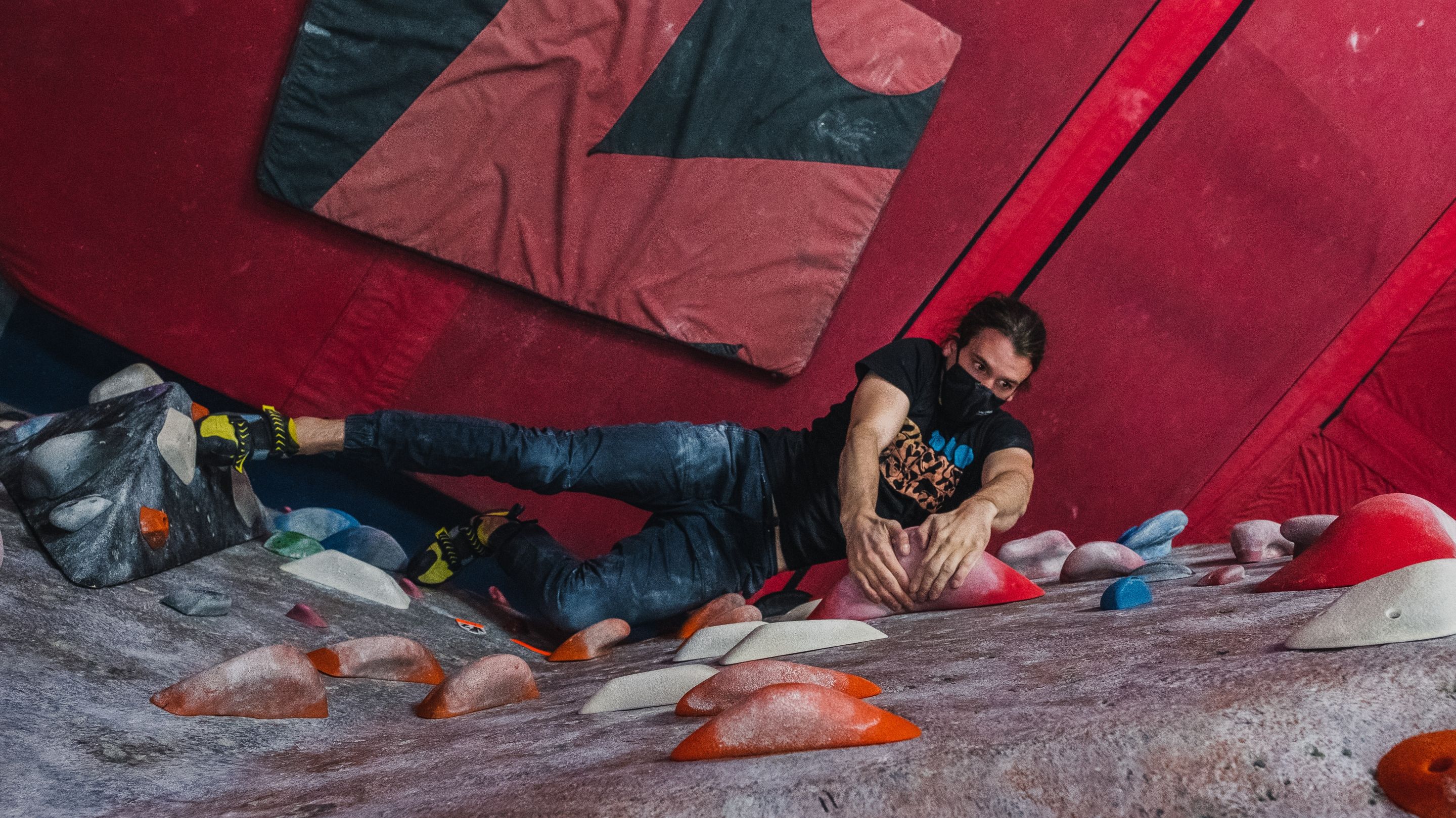 A from-above shot of a climber reaching for colourful holds inside a climbing gym.