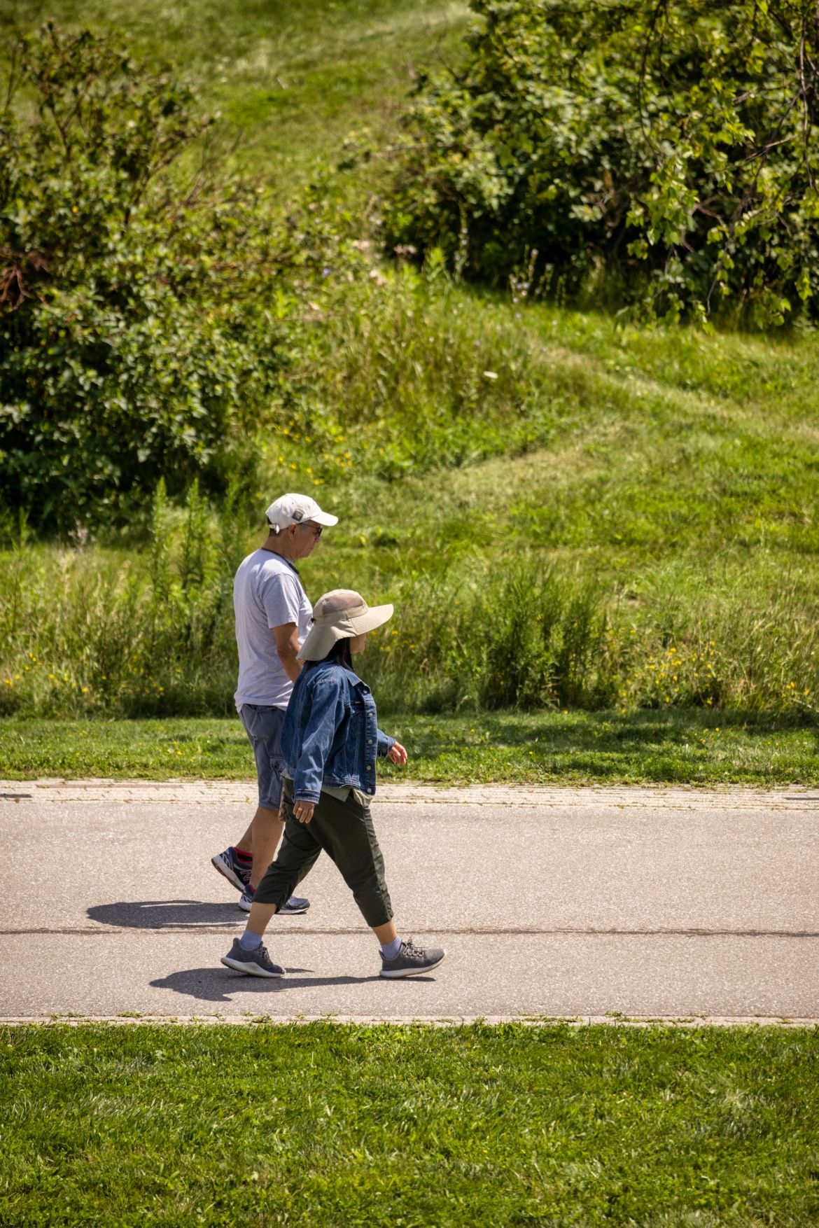 Two people walking side by side on a paved path, grass on either side.