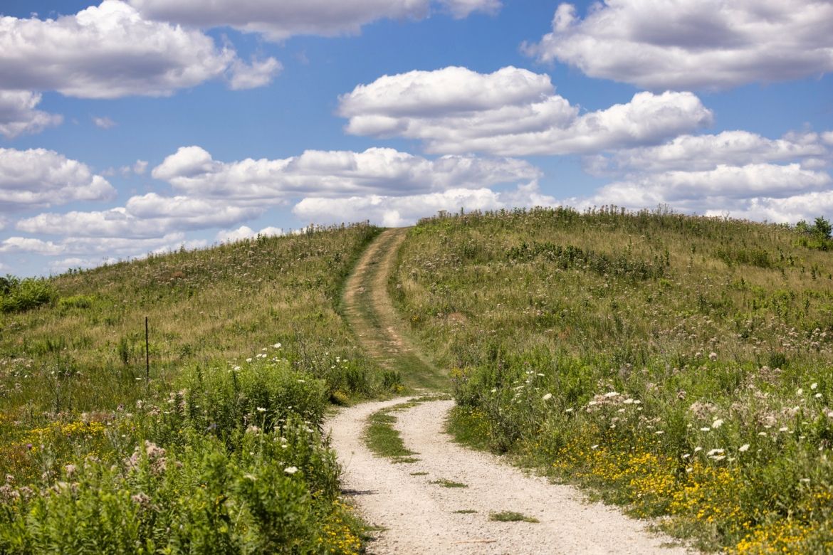 A path leading up a large hill. A cloudy sky in the background.