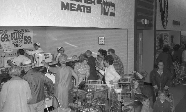 A black and white photo of customers gathered around a kosher deli.