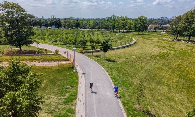 People walking on a path, grass on either side, and a blue sky in the background.