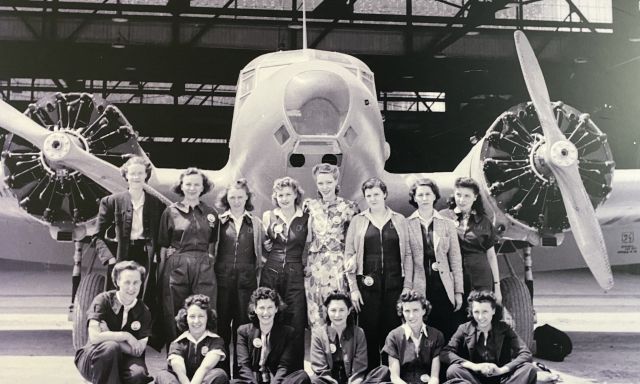 A black and white photo of a group of women posing in front of an aircraft.