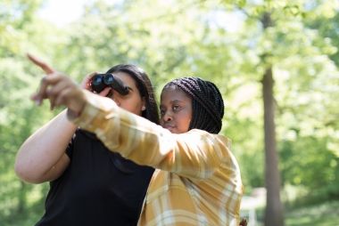 Two girls looking through binoculars in a forest.