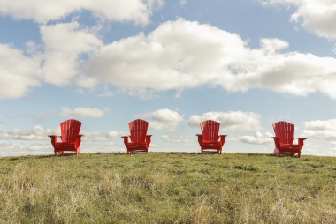 Four red Muskoka chairs on top of a hill.