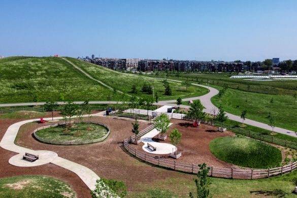 An aerial shot of Dogsview Park. Wooden fencing, grassy mounds, brown mulch, and a paved path.